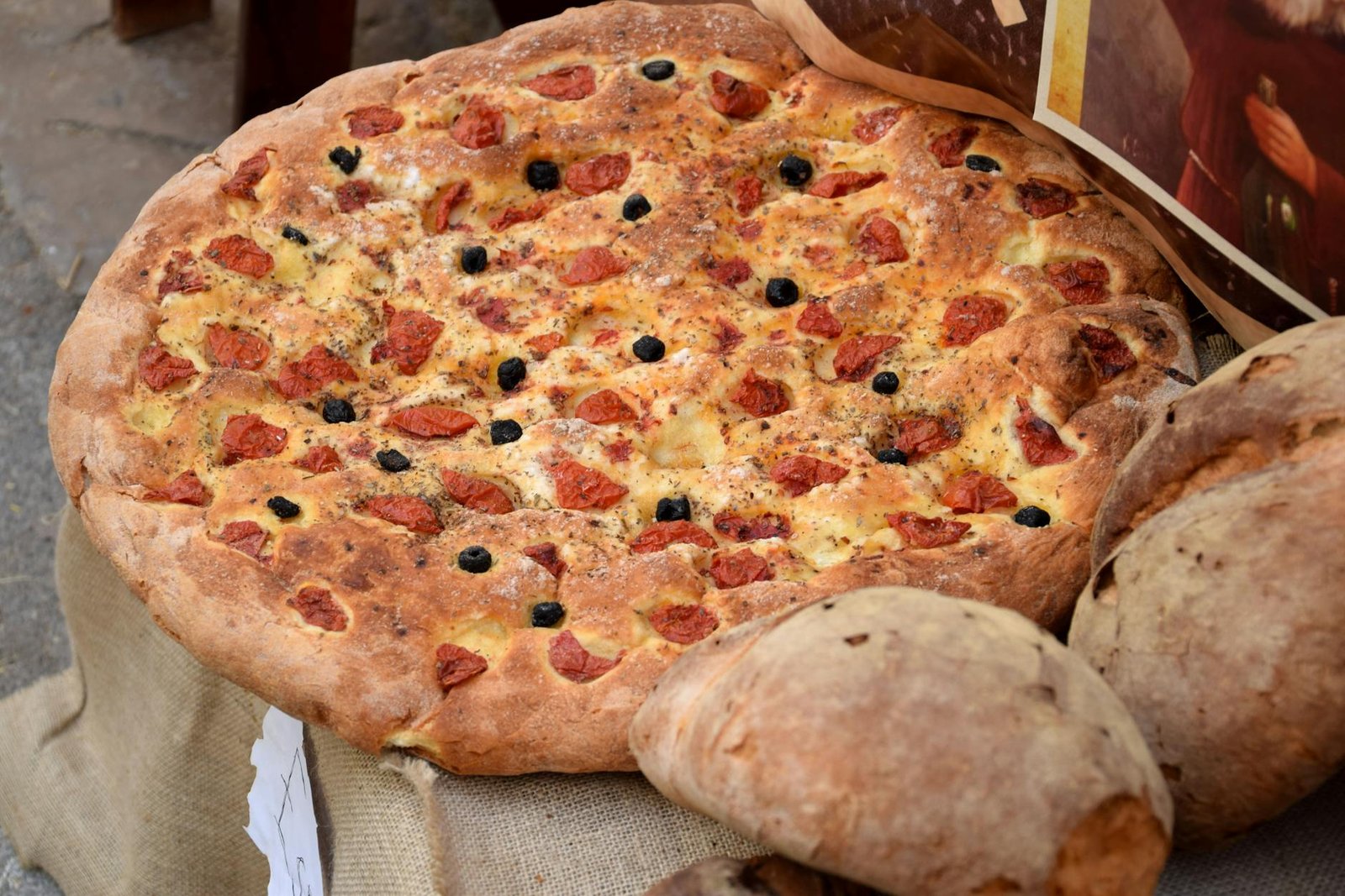 Freshly baked Italian focaccia topped with cherry tomatoes and black olives, showcasing rustic Mediterranean cuisine.