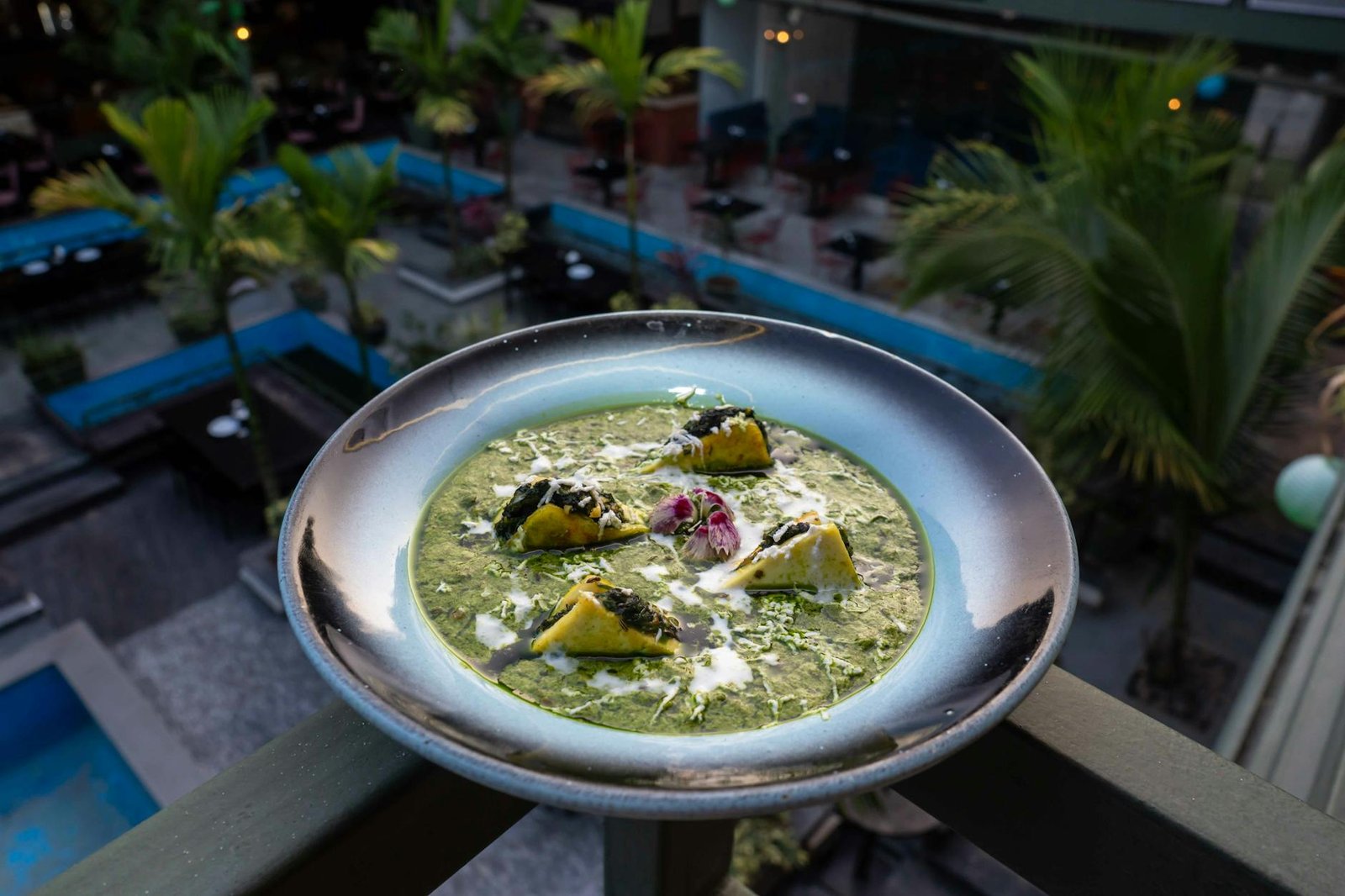 A gourmet Indian dish garnished with cream and spinach served at a rooftop restaurant with a tropical backdrop.