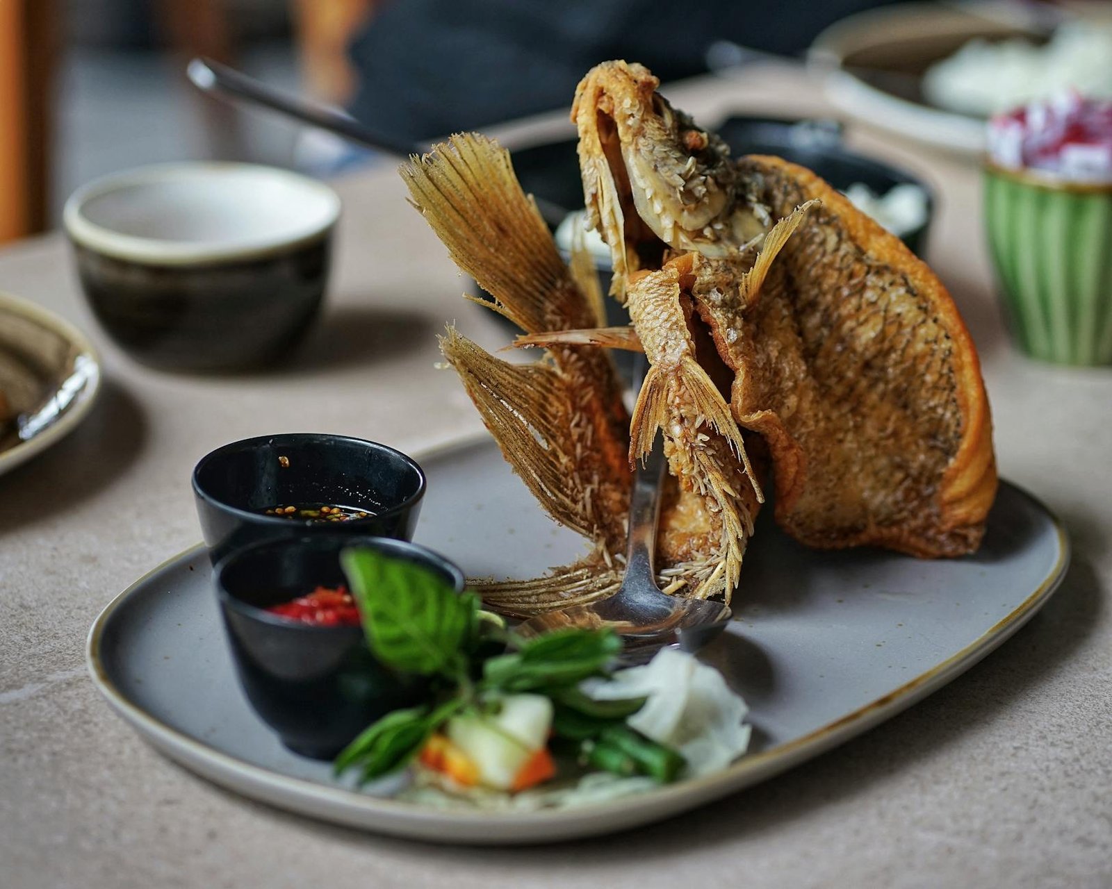 Crispy fried fish served with traditional Indonesian sides, garnished with herbs and fresh vegetables.