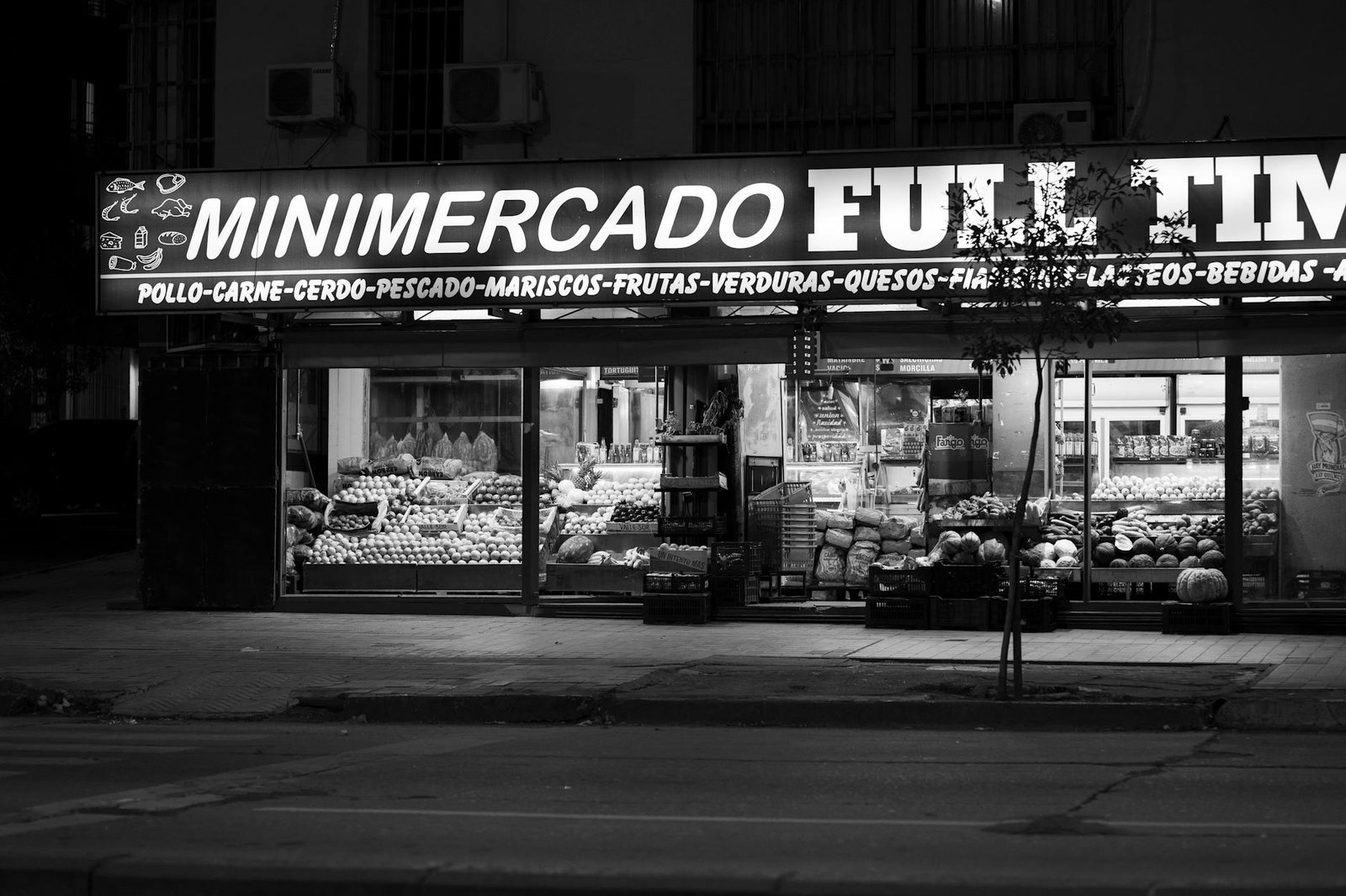 Monochrome nighttime capture of a minimarket in Córdoba, Argentina, showcasing fresh produce and groceries.
