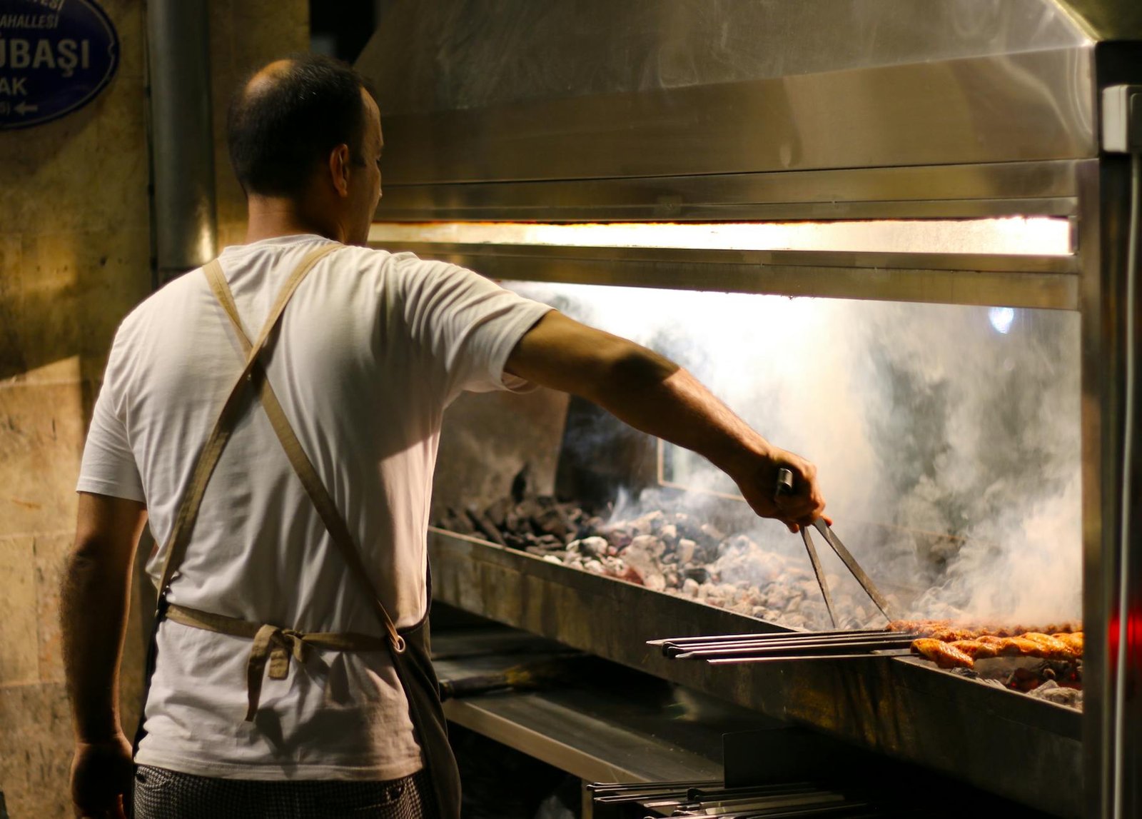 Chef grilling kebabs over open flame in a Gaziantep restaurant kitchen.