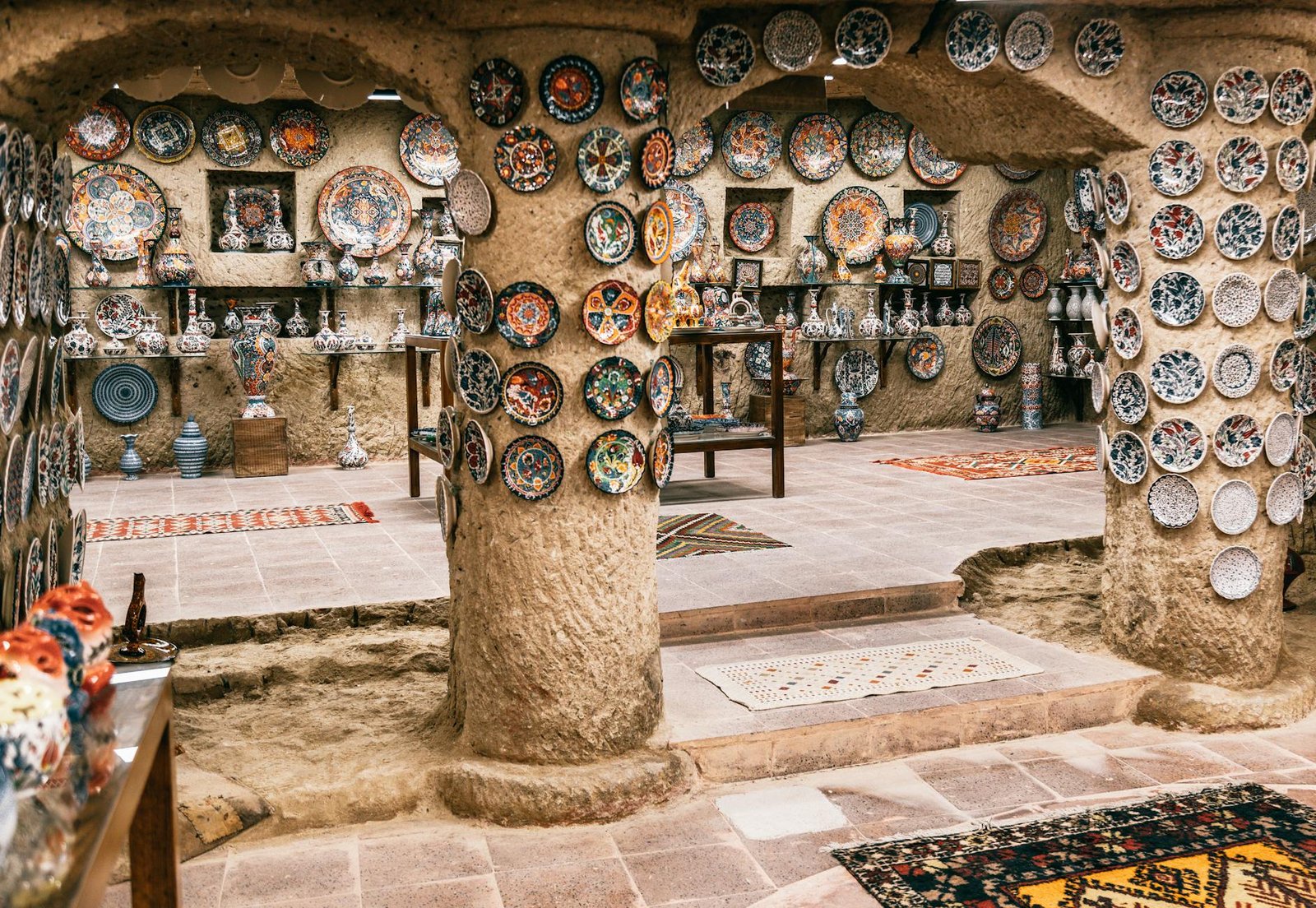 Moroccan plates hanging on rough stone walls and columns in building with carpets on floor