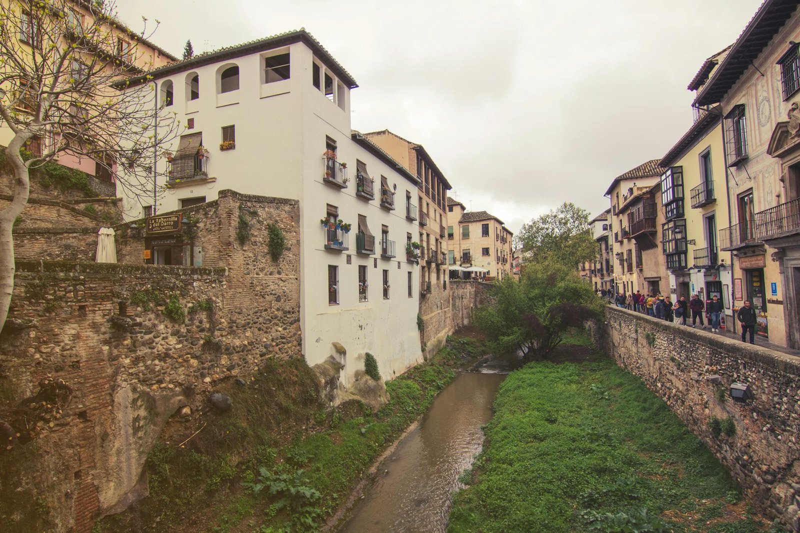 Picturesque street view of Granada's historic architecture alongside a serene river, capturing its timeless charm.