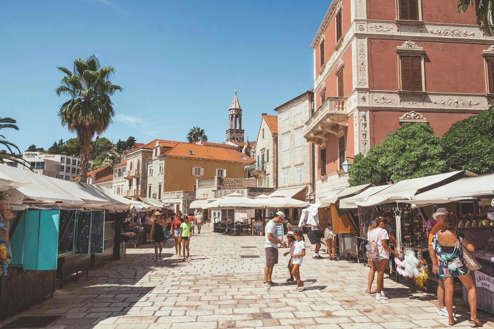 Vibrant market scene on a sunny day in Hvar, Croatia, featuring historic architecture and lively commerce.