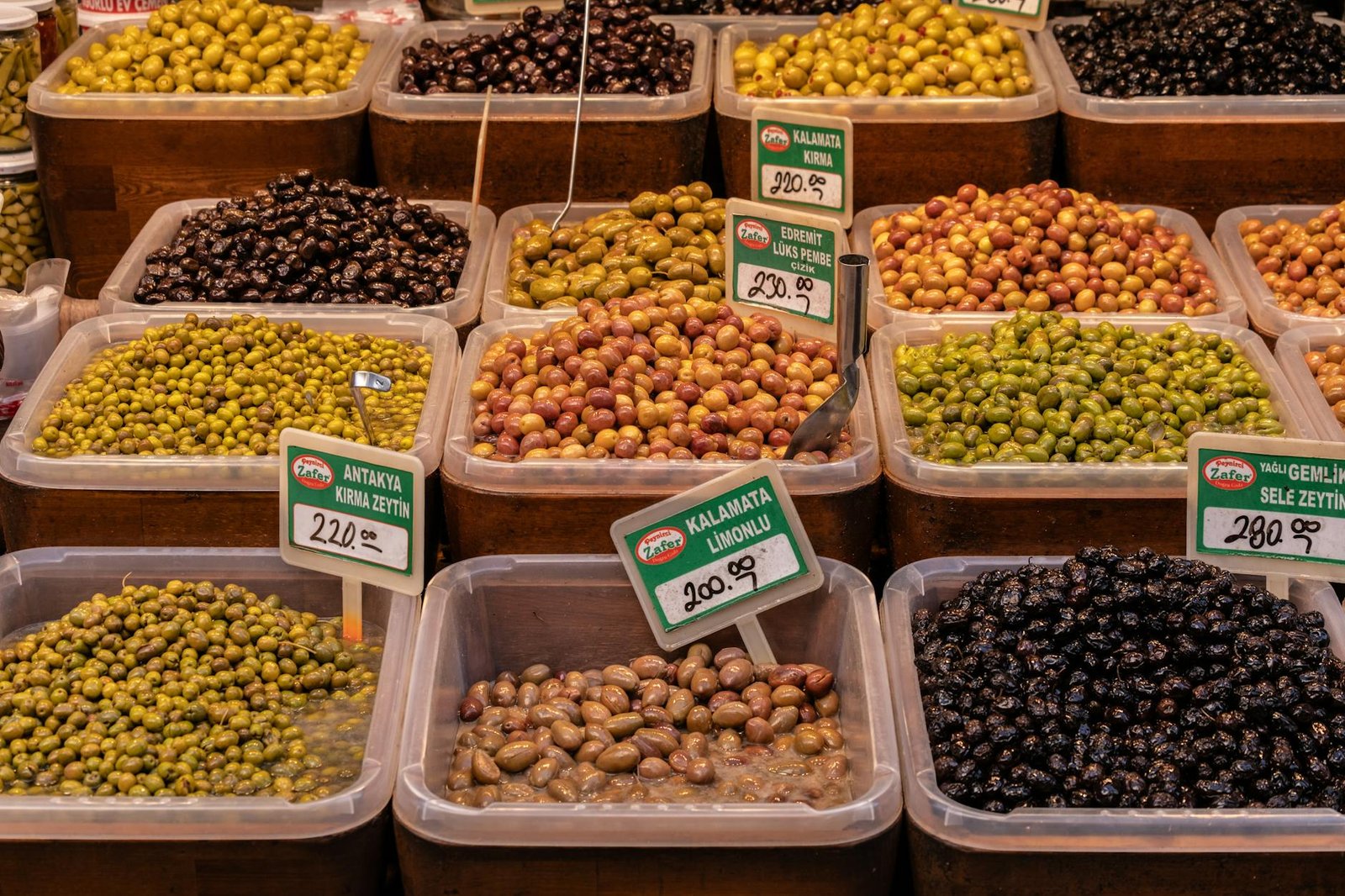Variety of olives in containers with price tags at a market in İzmir, Türkiye.