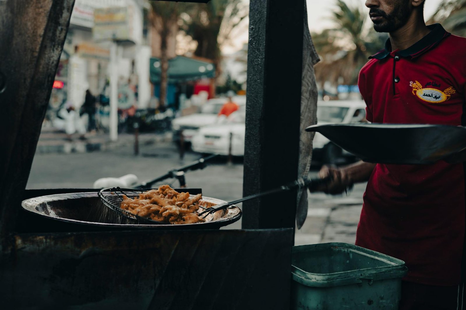 Street vendor frying crispy food outdoors in a lively city environment.