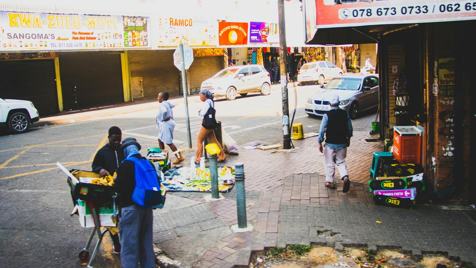 Bustling street corner in Johannesburg with people, cars, and market activities.