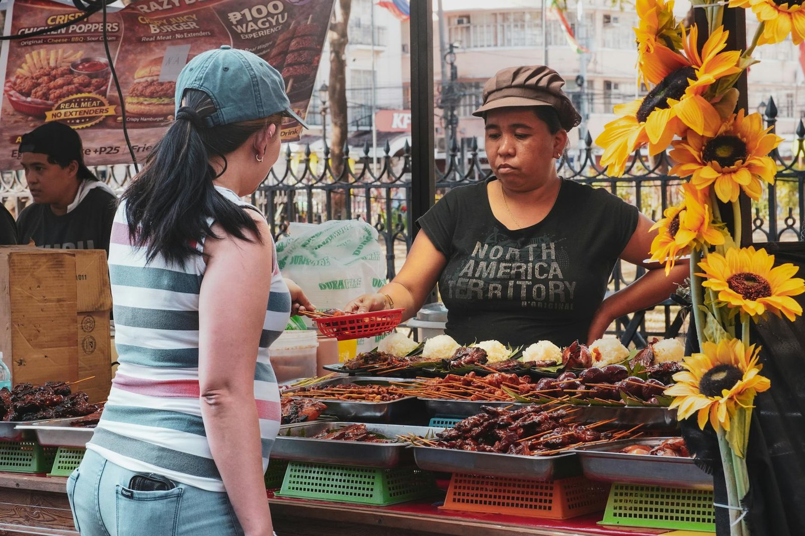 A street food vendor serves traditional Filipino skewers to a customer at a vibrant market in Manila, Philippines.