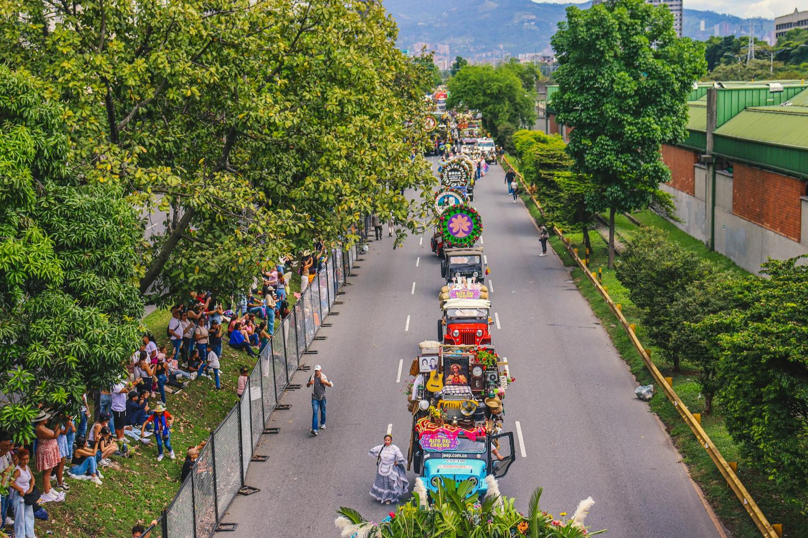 Vibrant parade scene during Medellín's Feria de Flores, showcasing decorated jeeps surrounded by lush greenery.