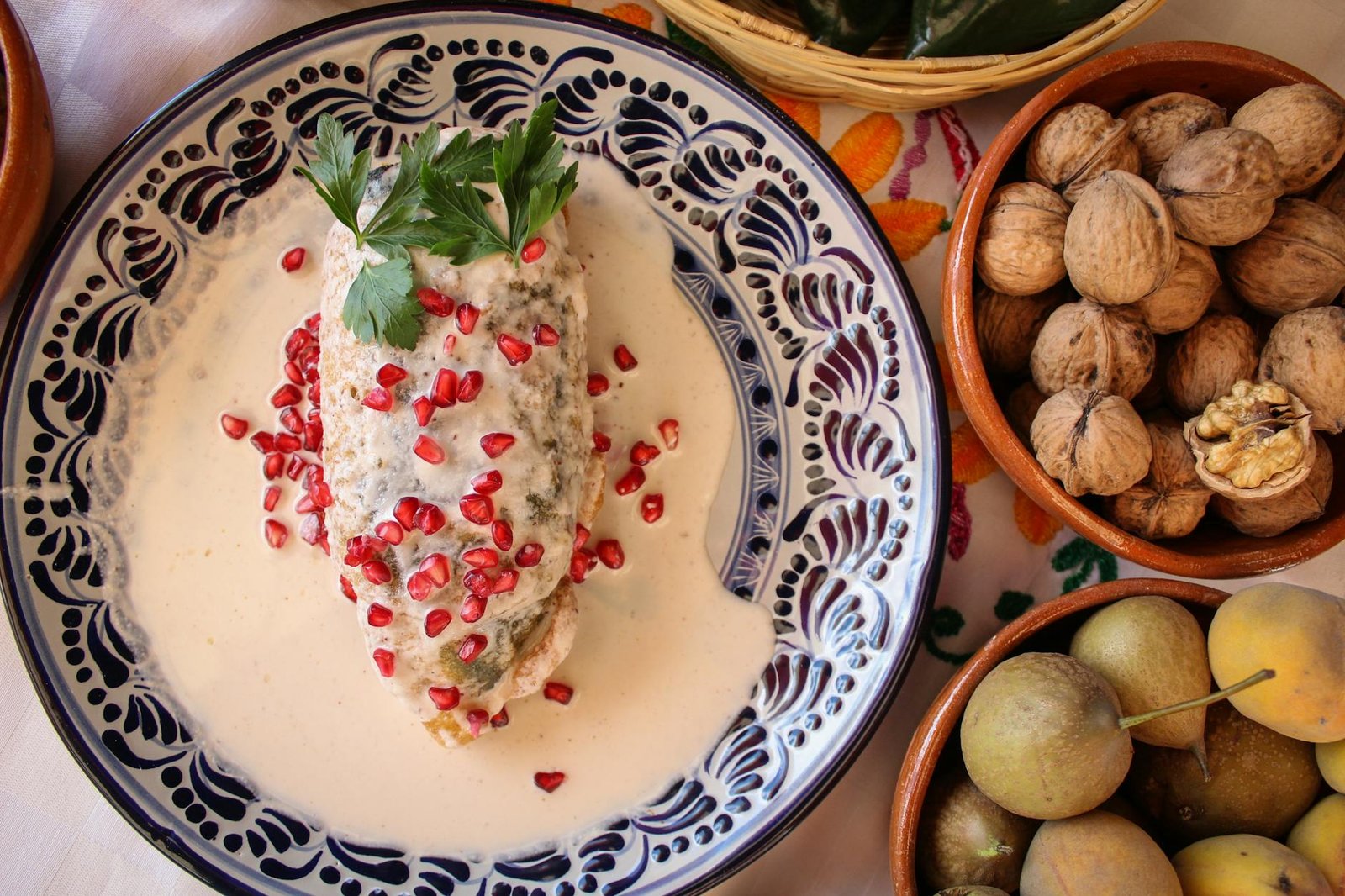 Traditional Mexican dish Chile en Nogada with pomegranate, nuts, and fruits, beautifully presented on a decorative plate.