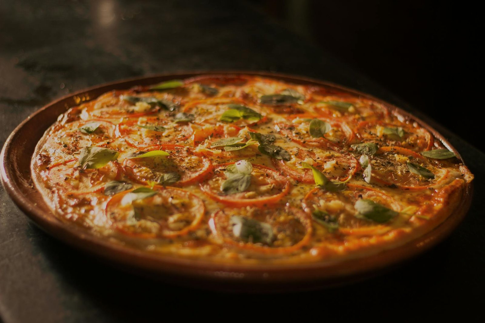 Close-up of a mouth-watering pizza topped with fresh basil, tomato, and mozzarella, capturing the essence of Italian cuisine.