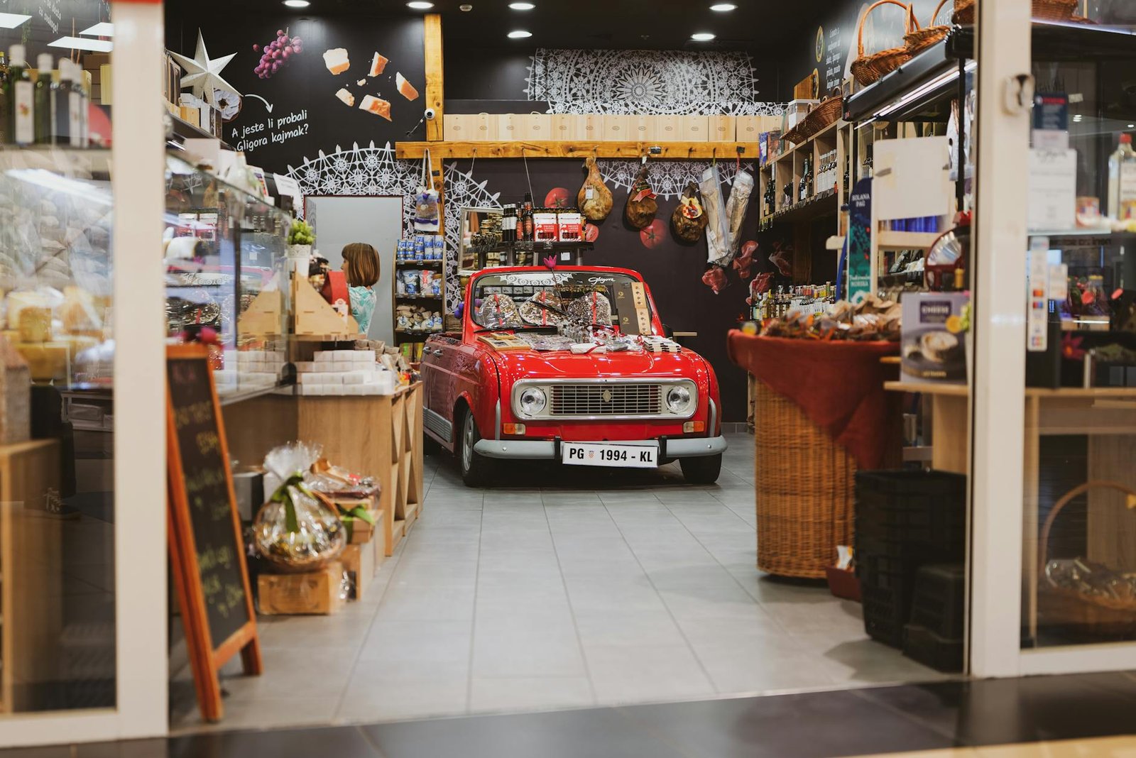 A vintage red car creatively displayed inside a cozy grocery store in Zagreb, Croatia.