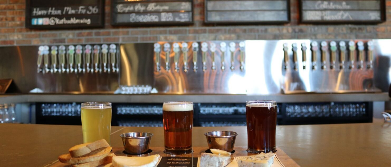 A selection of craft beers served with cheese and bread on a bar counter.